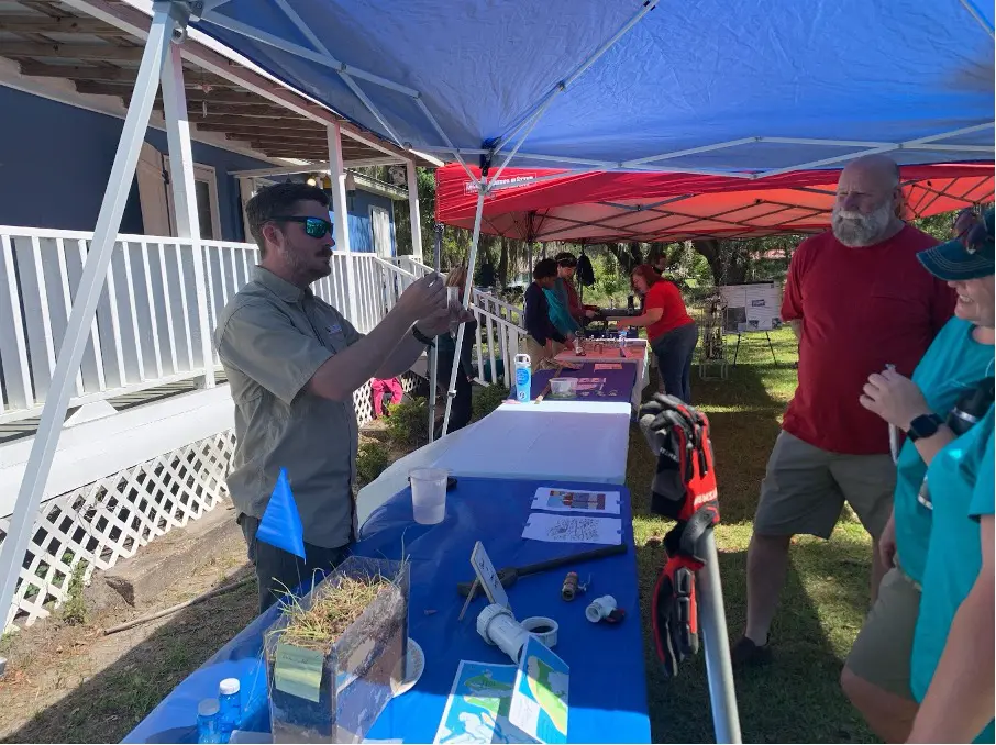 People listening to a presentation at a table under a tent.