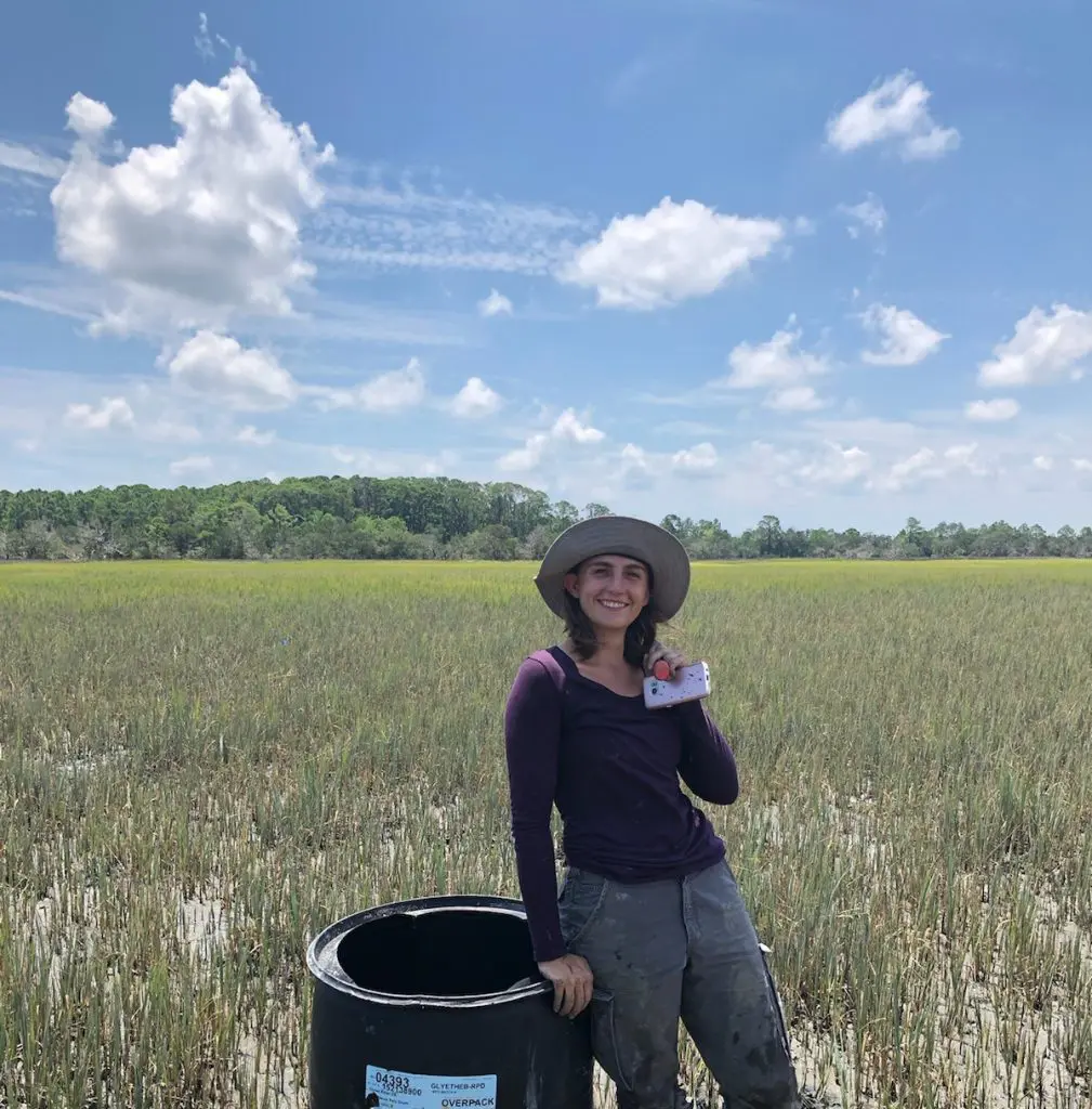 A young woman standing in a salt marsh with her experimental equipment