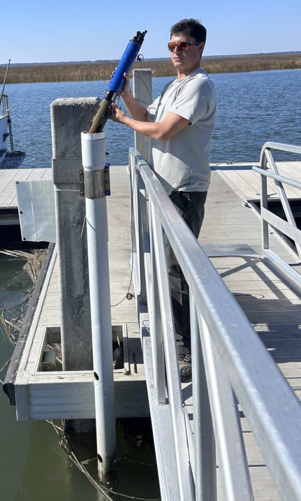 A young man putting a data sonde into a pvc tube on a dock